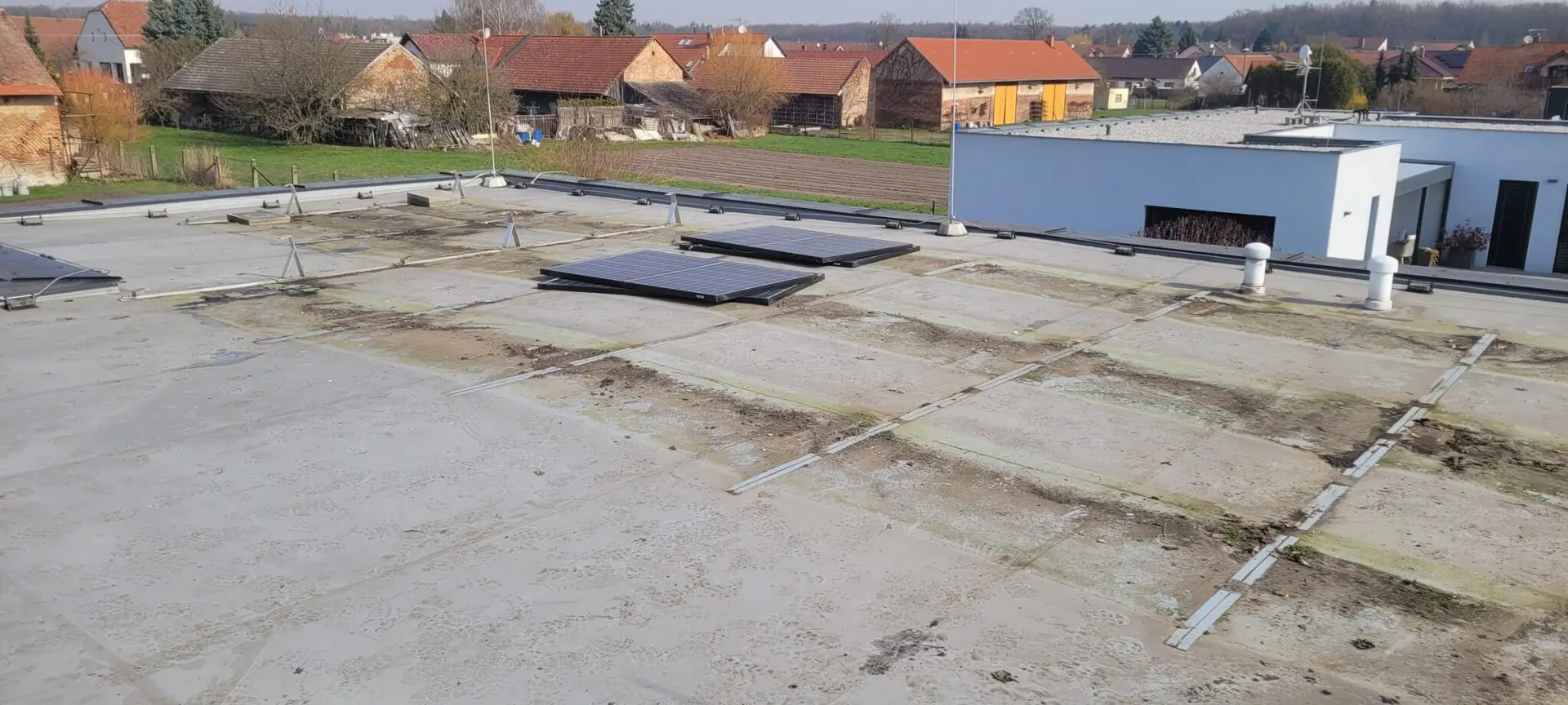 Pohled na plochou střechu v Pardubicích s částečně osazenou zátěžovou konstrukcí pro solární panely na betonové ploše.